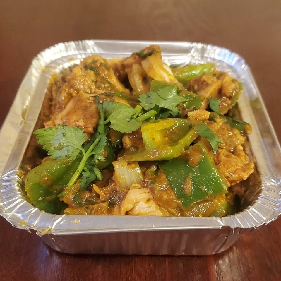 Spiced chicken and vegetables with green peppers, onions, and cilantro served in a foil tray on a wooden table.